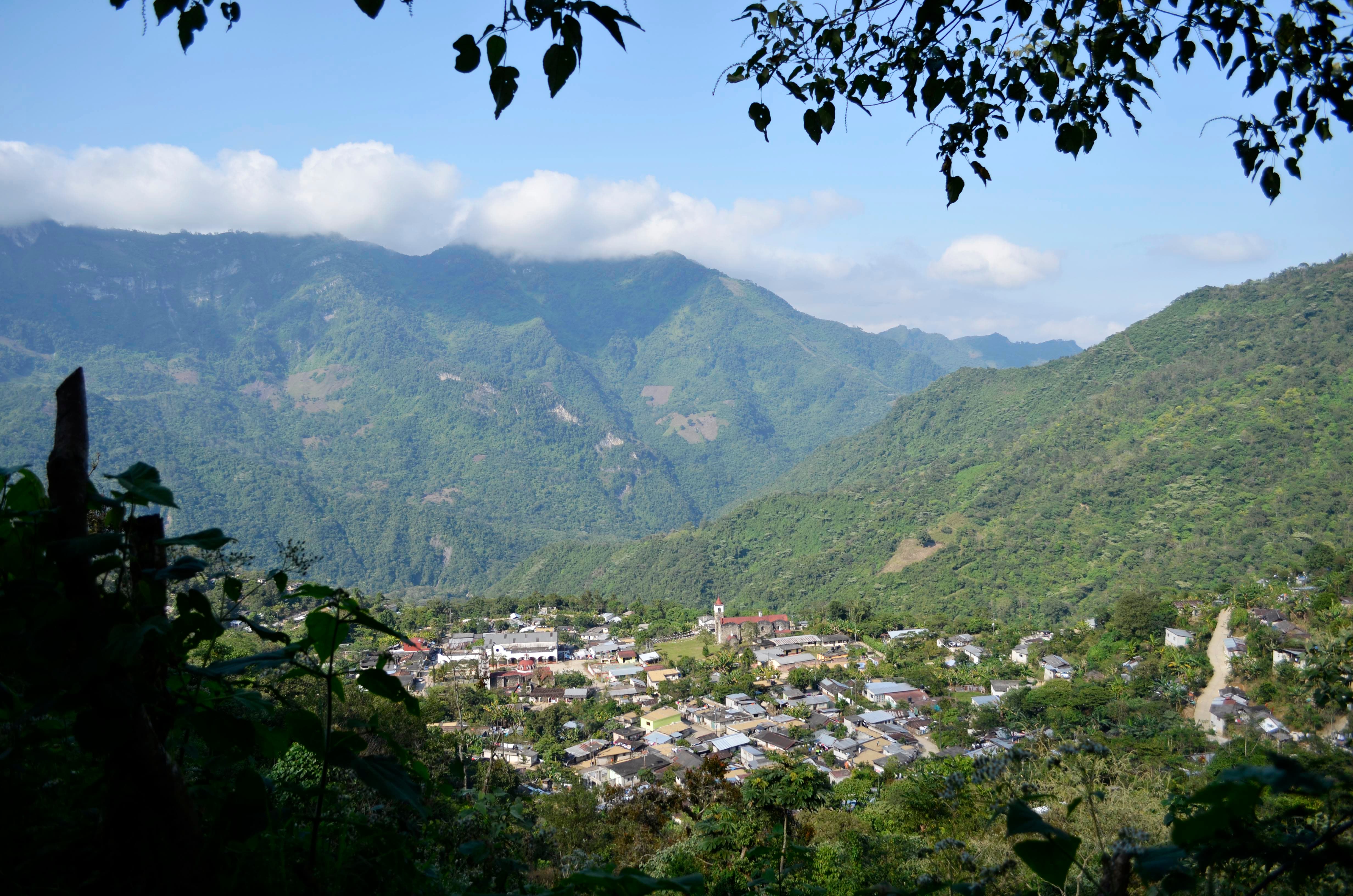 Mountain village beneath lush hills, framed by foliage, capturing the serene allure of Banyan Tree Puebla.